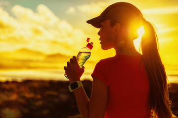 Fitness woman drinking water from sports bottle on afternoon workout after run training jogging...