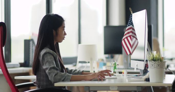 Young asian woman in a modern office, working at computer and check documents and information, side view.
