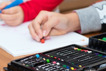 Set of crayons and markers with child hands drawing in background