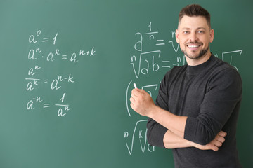 Handsome math teacher writing on blackboard in classroom