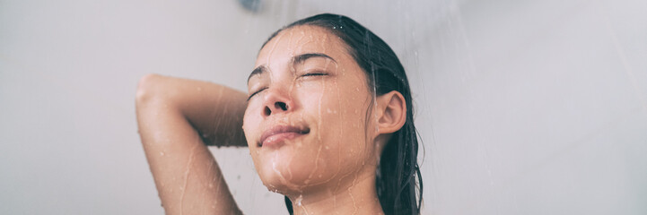 Shower woman taking hot bath rinsing hair in home bathroom. Asian girl under running water panorama banner header lifestyle. - obrazy, fototapety, plakaty