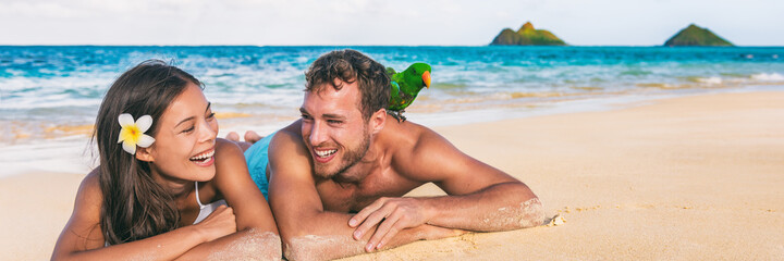 Beach people Hawaii honeymoon young couple laughing tourists with bird pet on shoulder -tourist attraction panoramic banner background, Lanikai, Oahu island, USA travel.