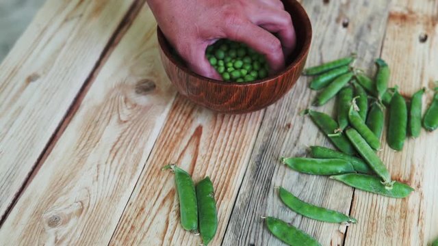 closeup of woman hand depod green peas in brown dish, on wooden table.