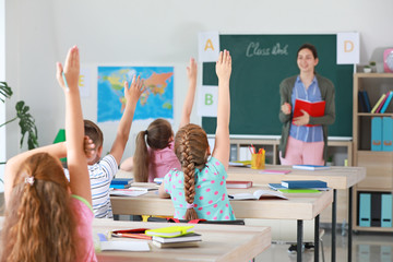 Cute little pupils raising hands during lesson in classroom