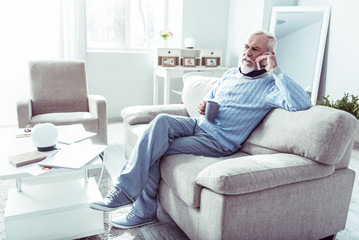 Obraz premium Stylish retired man holding his phone while calling wife from home
