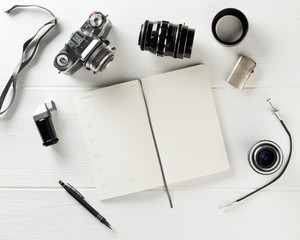 Retro analog film camera with notebook, pen and photography equipment on white wood table...