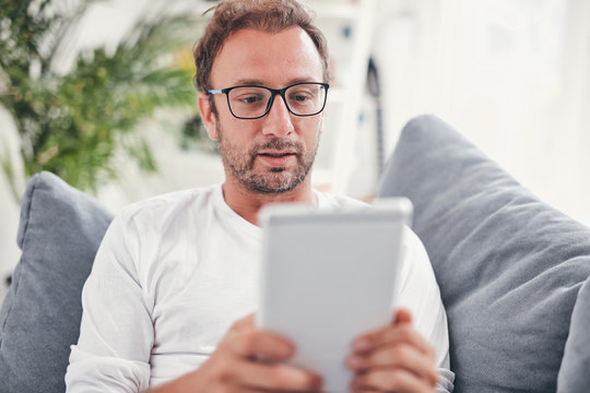 Man using tablet and sufring on the internet in his living room.