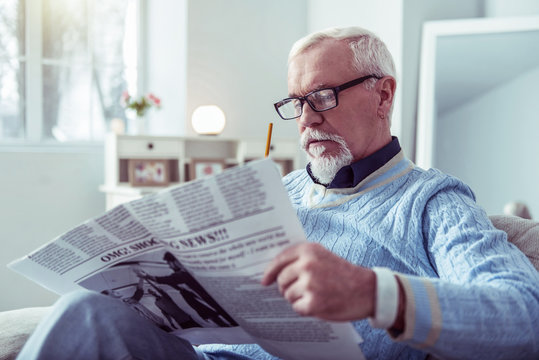 Bearded grey-haired man with earring in his ear watching morning newspaper