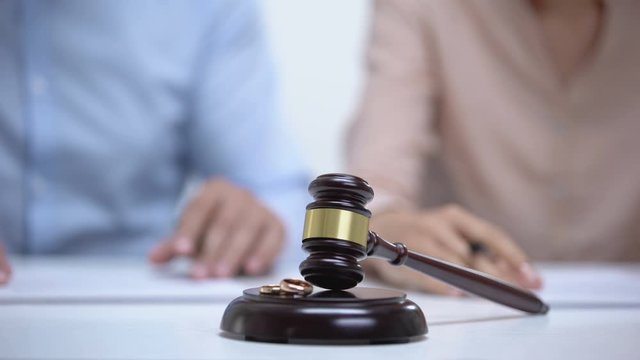 Marriage rings and gavel closeup, spouses signing divorce document on background