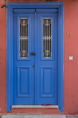 Blue wooden door with two small windows. Terracotta wall. Number plate next to the door.