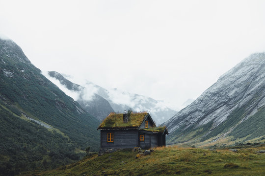 Norwegische Holzh&uuml;tte mit Nebelschwaden und Bergen im Hintergrund 