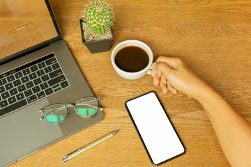 Businessman hand holding coffee cup with laptop and eyeglasson wooden desk.