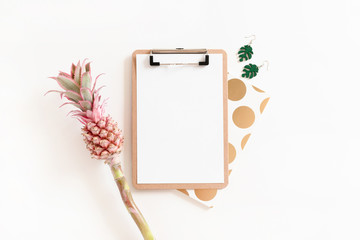Flatlay of clipboard mockup, notepad, earrings and pink pineapple on white background