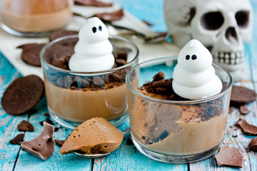 Halloween dessert for kids - delicious chocolate mousse with chocolate cookie crumbs and meringue ghost in glass on table with festive halloween decorations