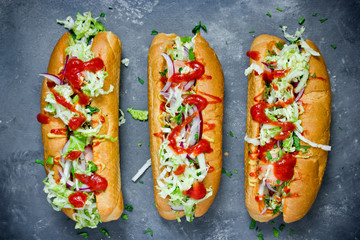 Hot dog with sausage, cucumber, cabbage and tomato sauce on dark slate background top view