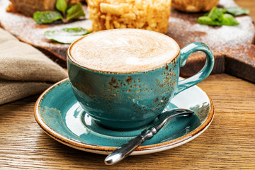 Cappuccino Cup with latte on wooden background. Beautiful foam, green ceramic Cup.