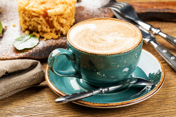 Cappuccino Cup with latte on wooden background. Beautiful foam, green ceramic Cup.