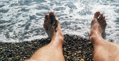 Men's feet on a pebble beach by the sea