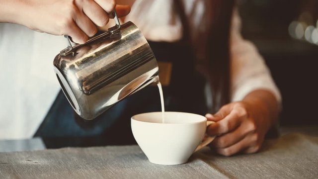 Asian professional female barista pouring milk in latte art coffee at counter bar in cafeteria restaurant as shop owner. Waitress girl making coffee. People lifestyles and occupation job. 4K footage