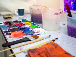 Artist tools, paint brushes, white bucket of water and acrylic colour artist palette in art studio.