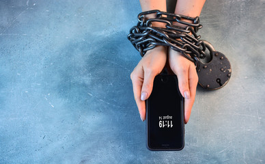 Smartphone addiction of modern people concept with hands tied with metal chain and lock.