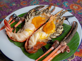 Roasted grilled giant river shrimp or prawn on green banana leaf on.vintage white zinc dish on beautiful fabric Thai style. Thai style food with Thai decoration concept.