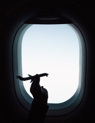Child playing by aircraft window in silhouette