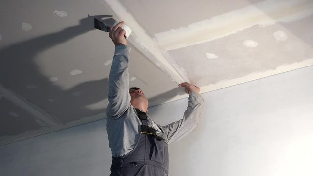 Worker glue glass fiber tape on ceiling plasterboard joint