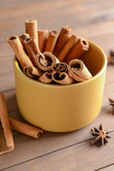 Bowl with aromatic cinnamon sticks on wooden background