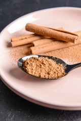 Spoon with cinnamon powder and sticks on plate, closeup