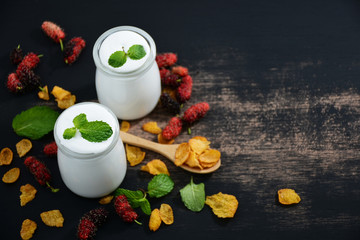 Breakfast yogurt in a glass bottle with a spoon and mulberry balls on a black old wooden floor.