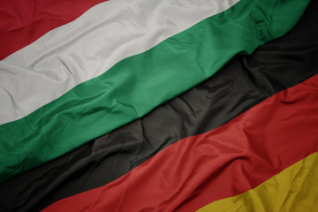 waving colorful flag of germany and national flag of hungary.