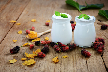 Breakfast yogurt in a glass bottle with a spoon and mulberry balls on the old wooden floor