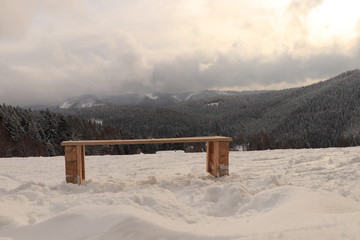 Wonderful winter atmosphere on Beskydy mountains. Wooden homemade bench settled in a snow cover. White and grey huge clouds rolling through the mountains