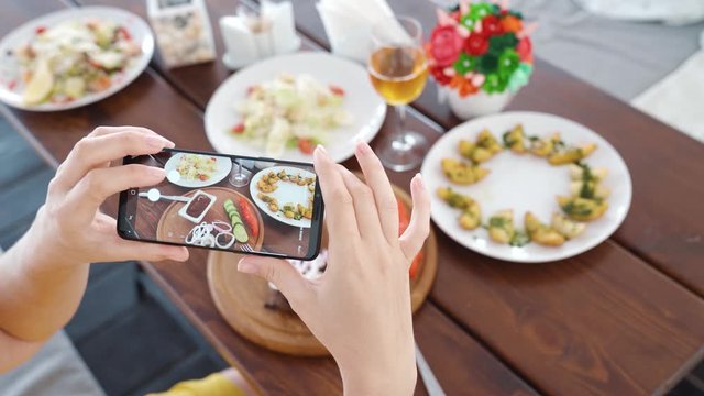 Food blogger hands using smartphone taking photo of beautiful beef steak on wood table inside the cafe to share on social media. Top view food photo. Lifistyle concept. Videoshot of people on vacation