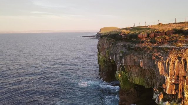 AERIAL DOLLY IN Flying alongside spectacular rock shelters under Carrowmore Lacken cliff at sunset
