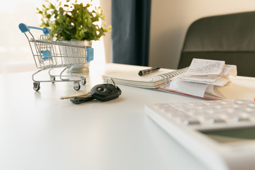 Car purchase concept. Empty shopping cart , car keys, calculator and notebook  on white table