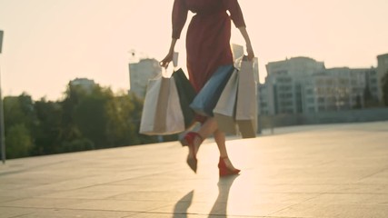 Young woman in red dress with shopping bags walks on the street during sunset - Powered by Adobe