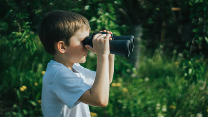 Little boy looking trough a binoculars in a park. Exploring the world. Summer holidays. Outdoor activities.