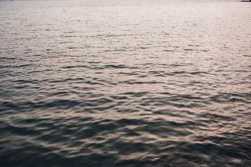 Sea or ocean water with little relaxing waves and reflection in different light. Beautiful gradient with creamy pink and dark blue colors. Neutral background and texture.