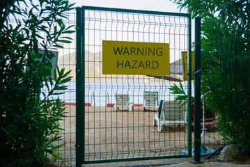 Closed beach. Biological hazard or disaster. Abandoned sunbeds behind bars with warning sign