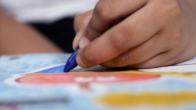 Closeup shot of an Indian child / kid coloring with a blue crayon in his drawing book. 