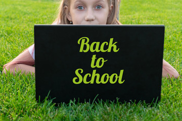 Portrait of caucasian little girl behind laptop computer lies on the grass in the park. Pretty girl...