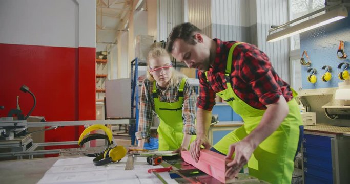 Carpenter teaching apprentice while working in joinery workshop. Transfer of experience