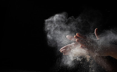 Obraz na płótnie Canvas woman chef hand clap with splash of white flour and black background with copy space.
