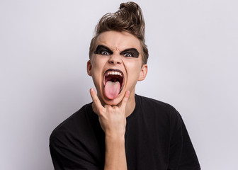 Crazy teen boy with spooking make-up making Rock Gesture on gray background. Teenager in style of...