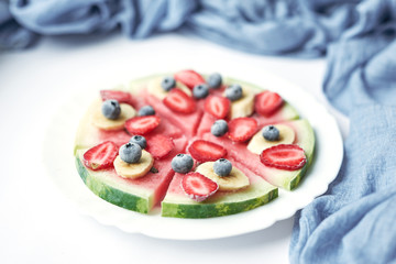 plate with vegan slices of frozen fruits: arbuk, blueberries, blueberries, banana with yogurt