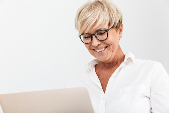 Image closeup of happy adult woman wearing eyeglasses smiling while using laptop computer