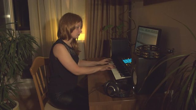 Home recording studio.  Young woman writes music using midi keyboard on computer. Then she listens to recorded result.
