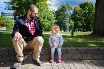 girl and her father sitting on a sidewalk